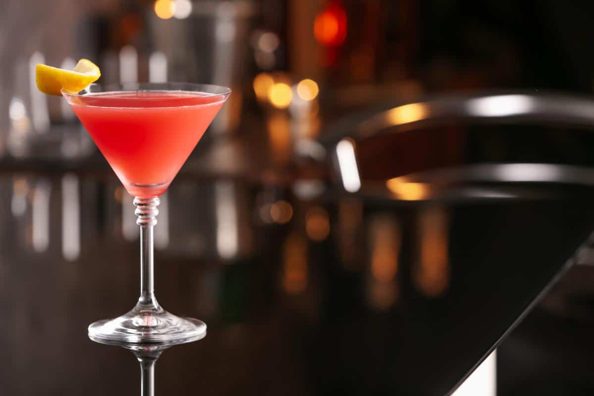 Pink cocktail in a martini glass with a lemon wedge garnish at a stylish bar.