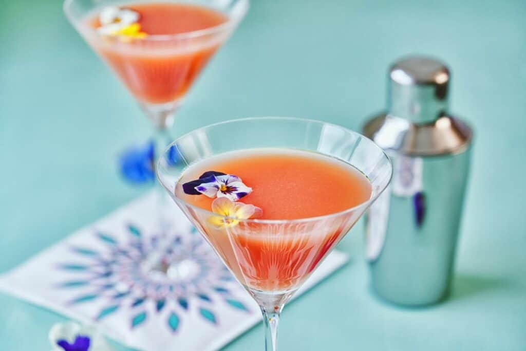 Vibrant pink cocktails garnished with edible flowers in martini glasses, perfect for mobile bar hire events in London and Berkshire. Stunning presentation of premium drinks for any occasion.