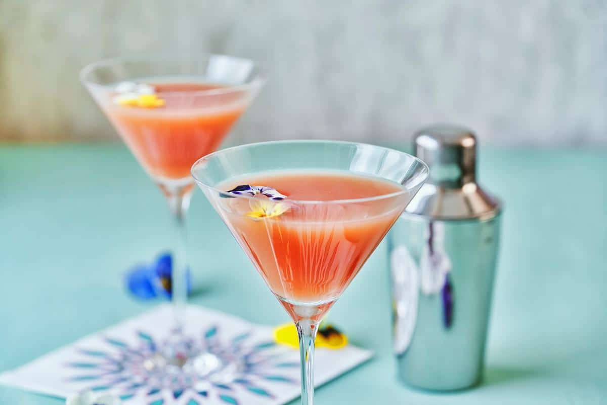 Elegant pink cocktails with edible flowers served in martini glasses, perfect for outdoor events.