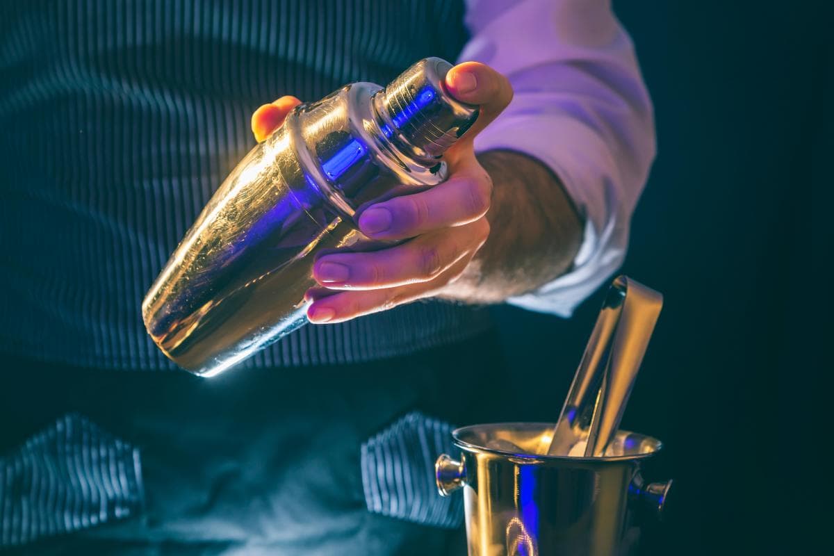 Shaker cocktail shaker on a bar, illuminated by colourful lighting, ready for cocktail mixing at an event.