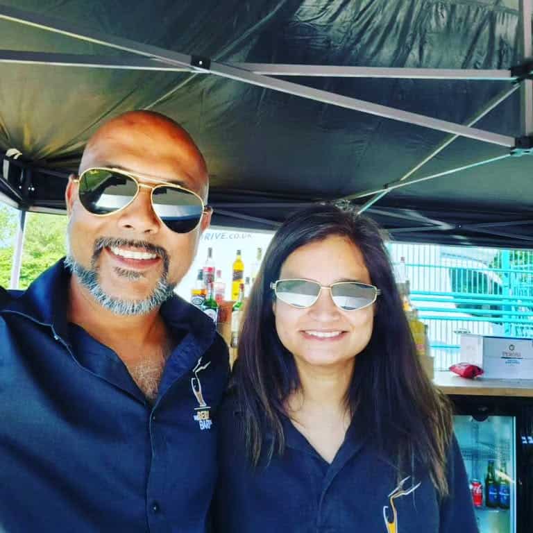 Vibrant photo of two smiling event staff wearing sunglasses at The Sesh Bars mobile bar hire, showcasing their friendly service at an outdoor event in London & Berkshire.