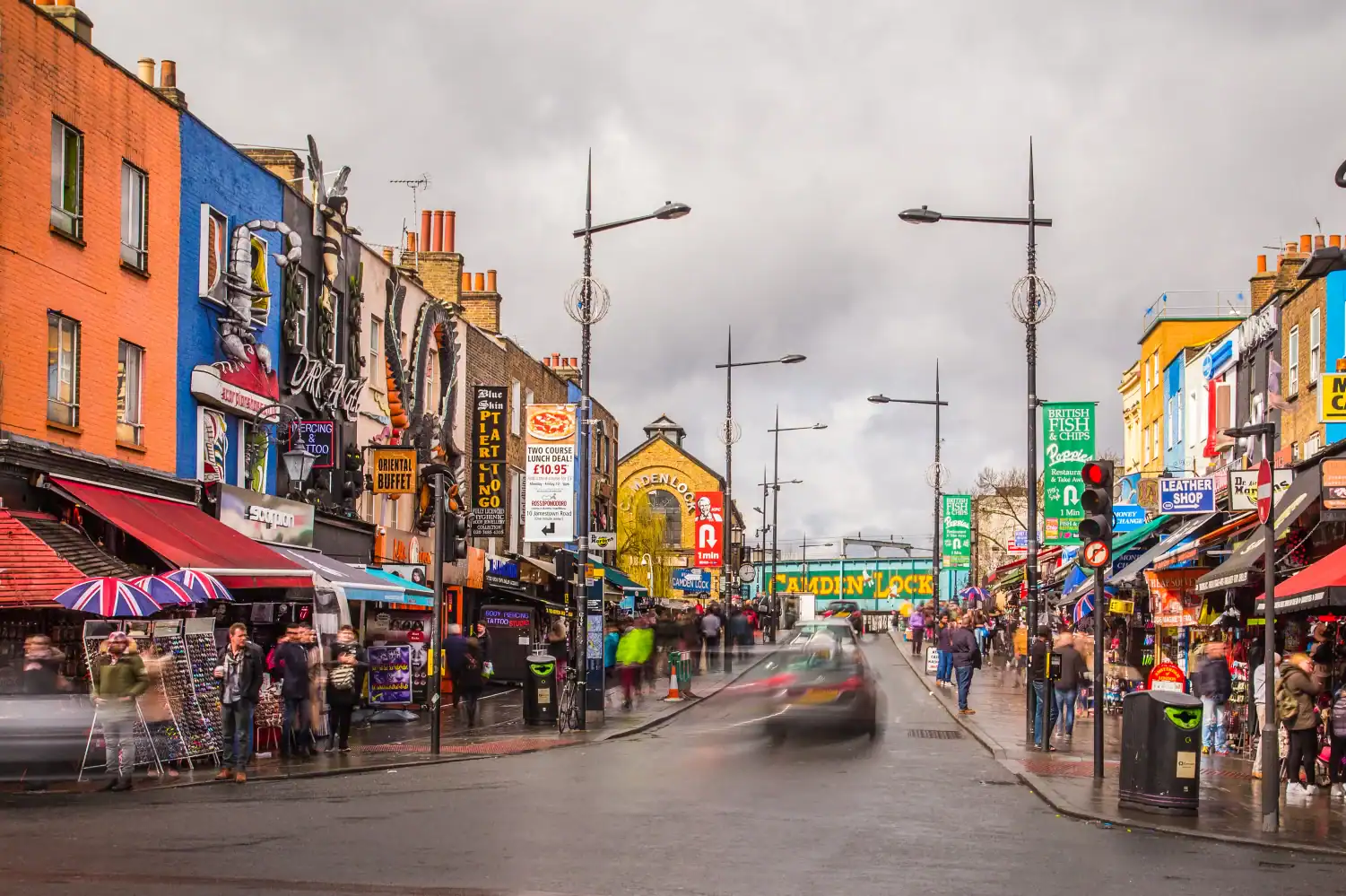 London street scene with lively shops, vibrant signage, and busy pedestrians under a cloudy sky, showcasing the energetic atmosphere of Camden Market.
