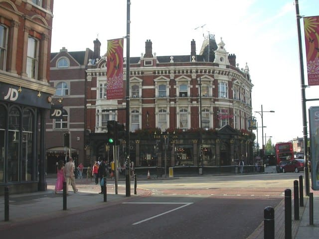 London street scene featuring a historic red brick building with ornate white detailing; vibrant atmosphere with pedestrians and traffic.