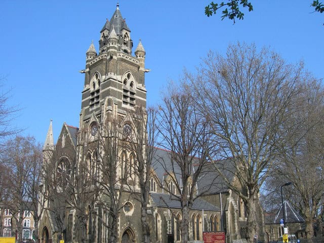 Church with gothic architecture and tall tower in London and Berkshire area, featuring bare trees and clear blue sky.