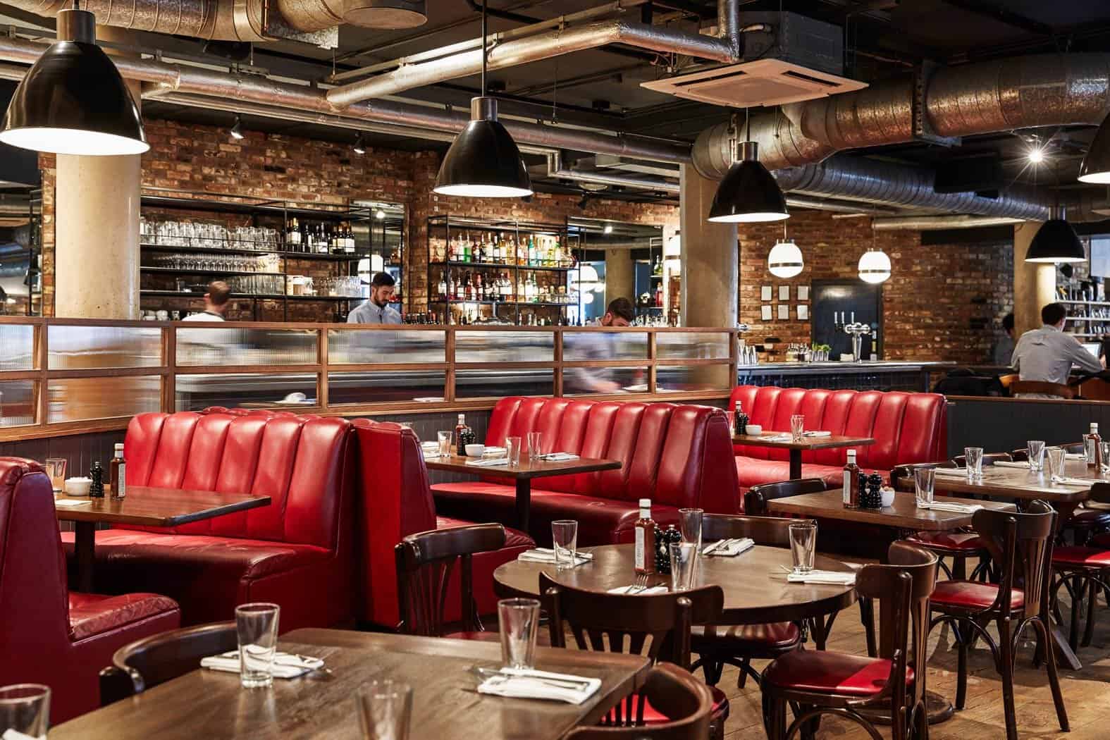 Spacious, stylish restaurant with red leather booths, wooden tables, modern lighting, and an industrial brick interior, ideal for events provided by The Sesh Bars Mobile Bar Hire London & Berkshire.