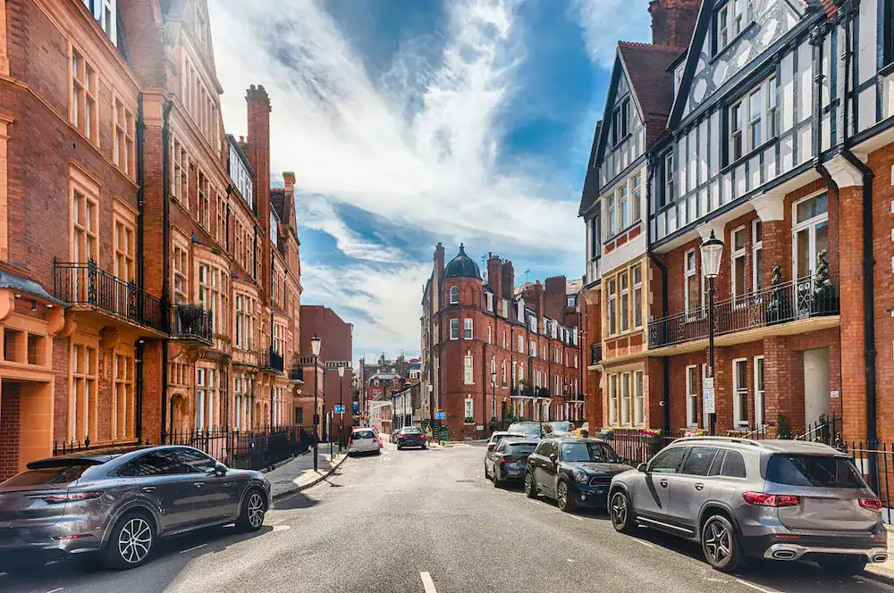 Elegant Georgian-style buildings along a charming street in London, featuring classic red brick facades and black wrought iron railings under a partly cloudy sky.